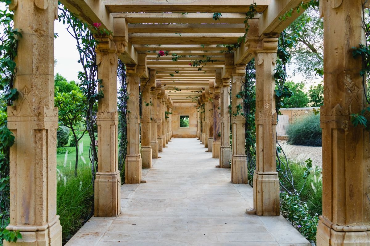 Kamena pergola obrasla ružama u uređenom vrtu